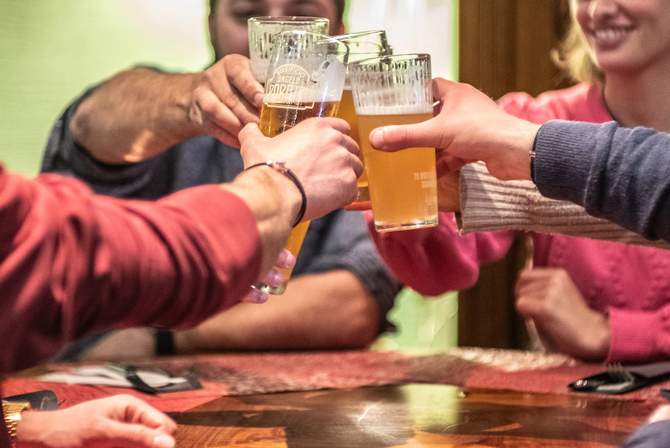 Una tavolata di amici brinda seduta al tavolo con della birre alla spina sapientemente spillate